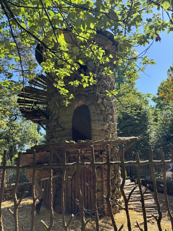 A small stone tower with a wooden fence around it and goats roaming inside the fence. 